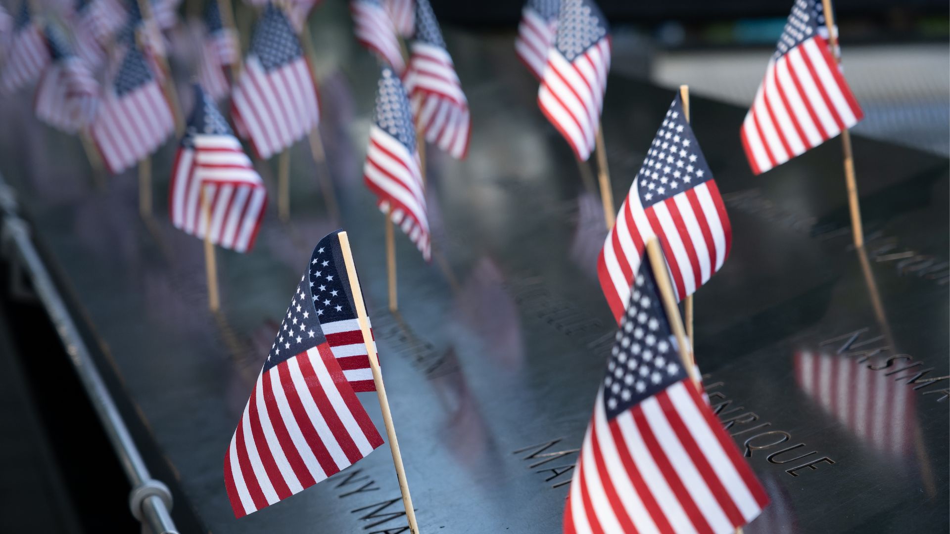 Small American flags wave atop engraved names on the Memorial
