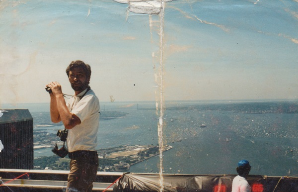 Stephen Knapp holds a pair of binoculars on the rooftop of the North Tower in this old photo. The South Tower can be seen off to the left. Aerial views of New York Harbor and the Atlantic Ocean are seen to the right.