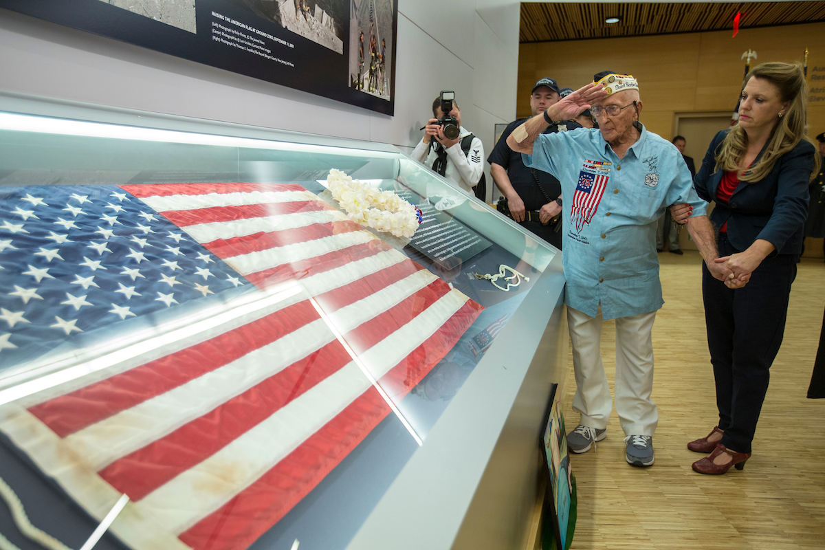 John Seelie, a U.S. Army veteran and Pearl Harbor survivor, salutes an American flag that flew at Ground Zero as he stands beside it at the 9/11 Memorial Museum.
