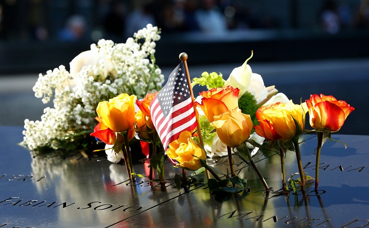 White, orange, and yellow flowers and an American flag are left as tributes are left on the Memorial plaza during the 18th anniversary ceremony in New York on Wednesday, September 11, 2019. 