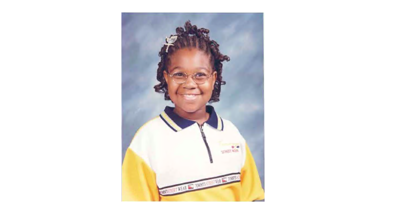 Asia Cottom, wearing a yellow polo shirt, smiles broadly for a yearbook photo.