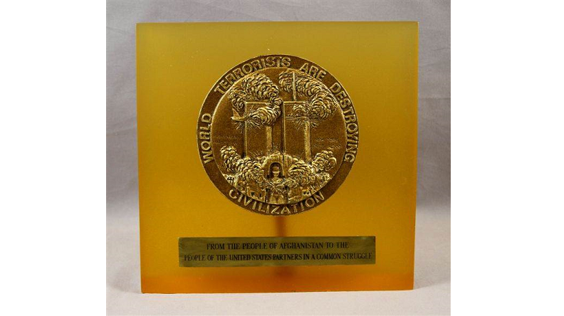 Orange-hued square plague with bronze seal in the upper center depicting the Twin Towers with smoke billowing out. Text written around the seal reads: "World terrorists are destroying civilization." 