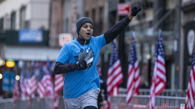 A man in winter running gear pumps his fist into the air as he approaches the finish line at the 9/11 Memorial & Museum's 5k Run/Walk.