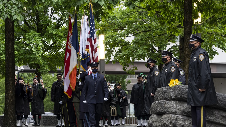 A photo of the May 30 commemorative moment held on the Memorial Glade. An honor guard procession carries an American flag on an overcast day.