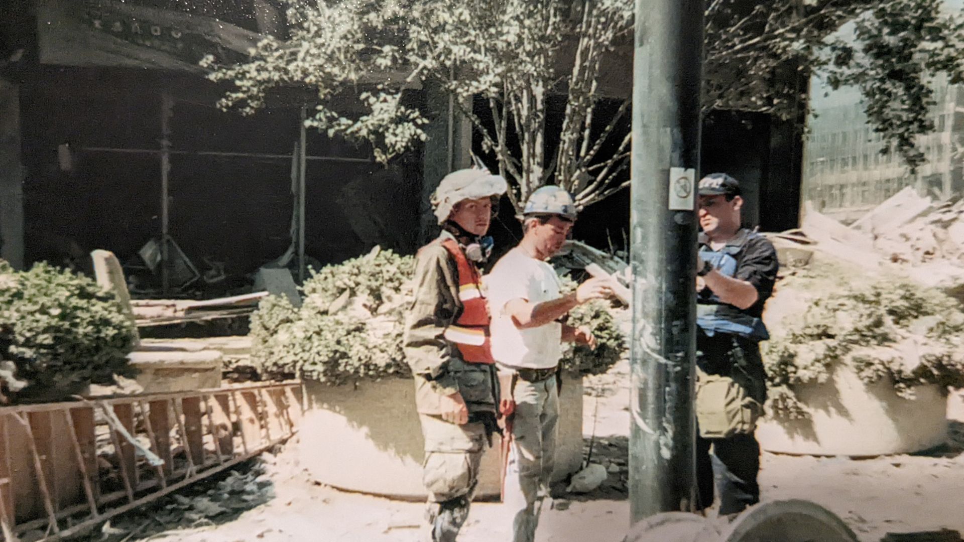 A man in a hard hat and one in army gear stand near a pole at Ground Zero
