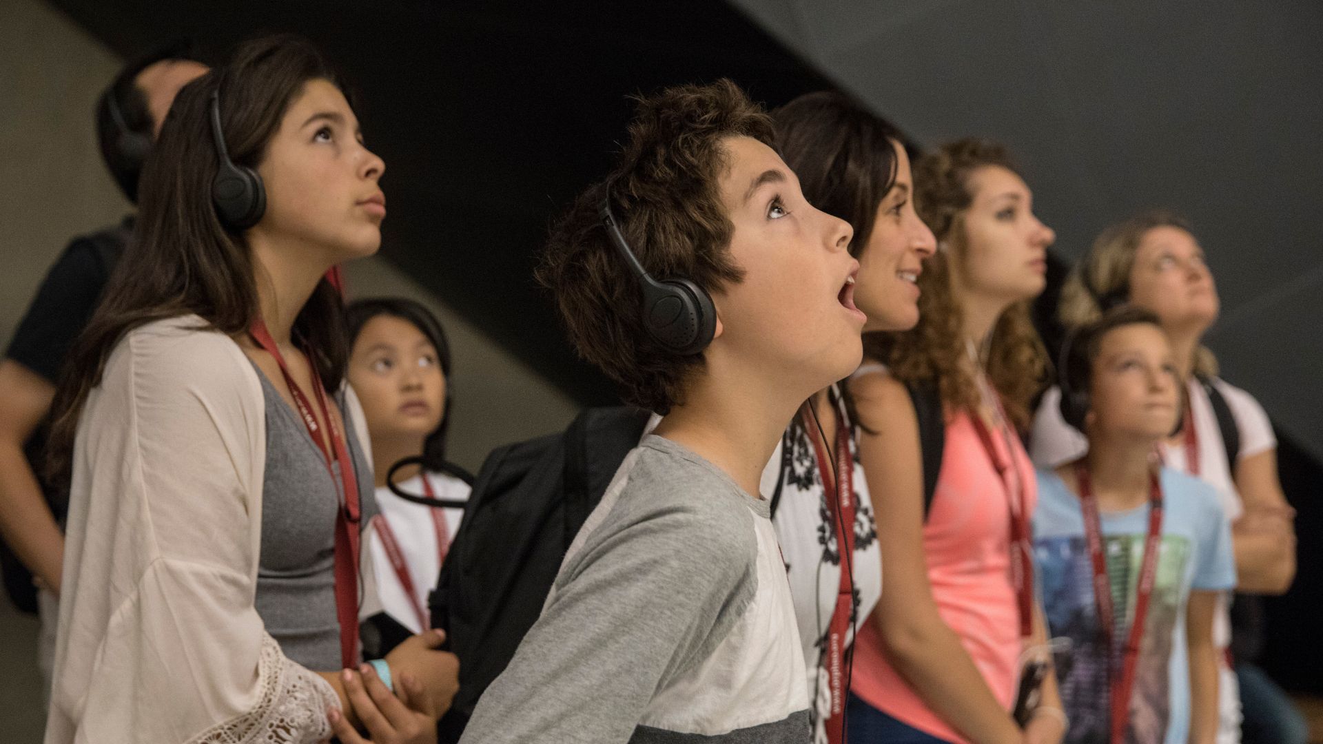 A small group of kids and adults wearing headphones look up in wonder