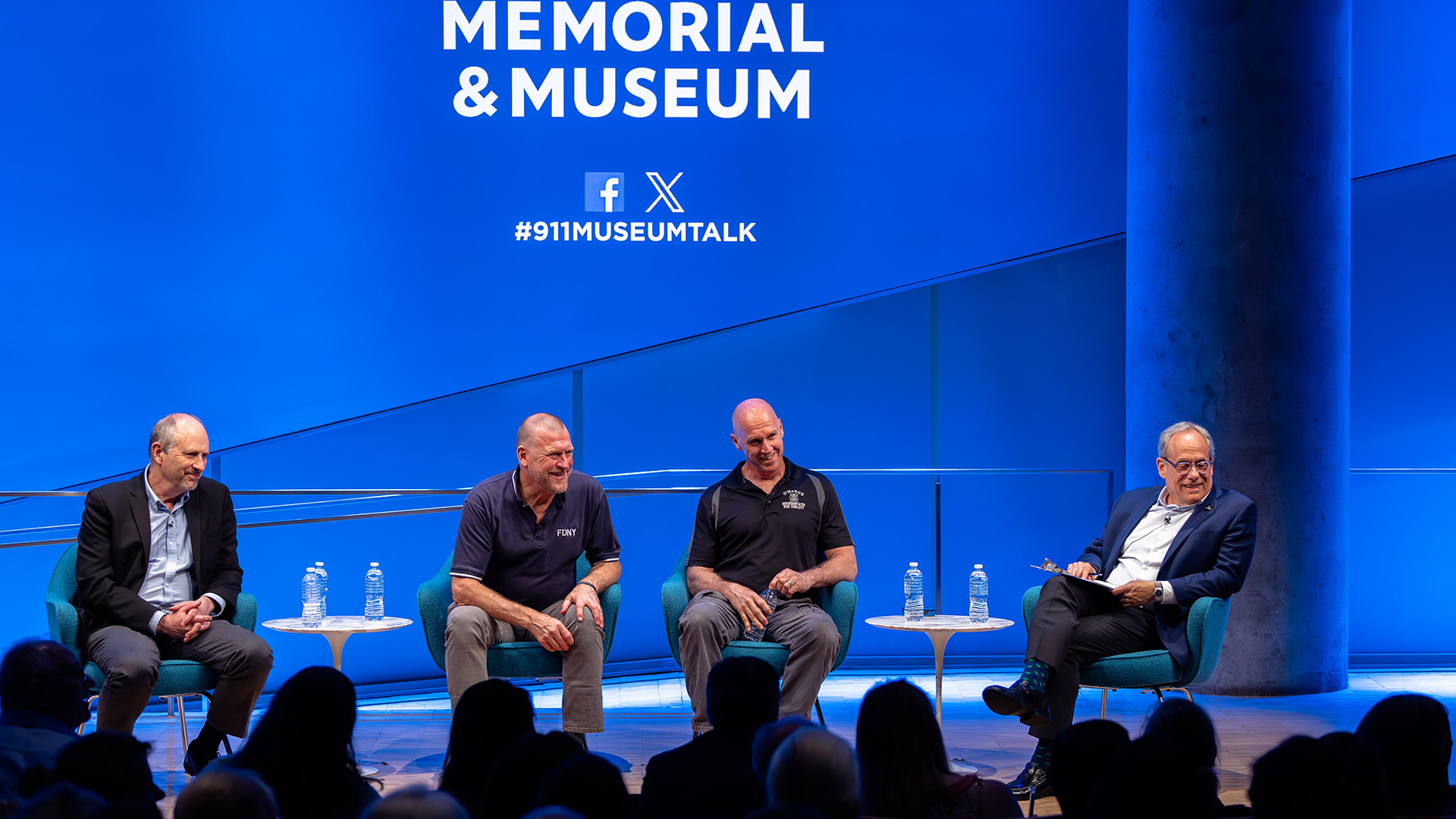 Four speakers sitting on stage, in front of the 9/11 Memorial and Museum #911MuseumTalk logo.