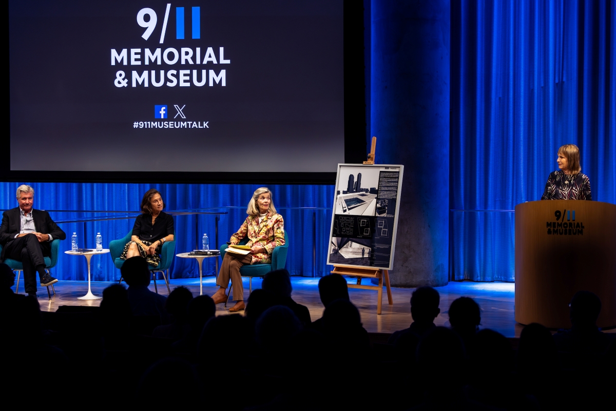 A speaker at the podium introduces the seated panelists on stage.