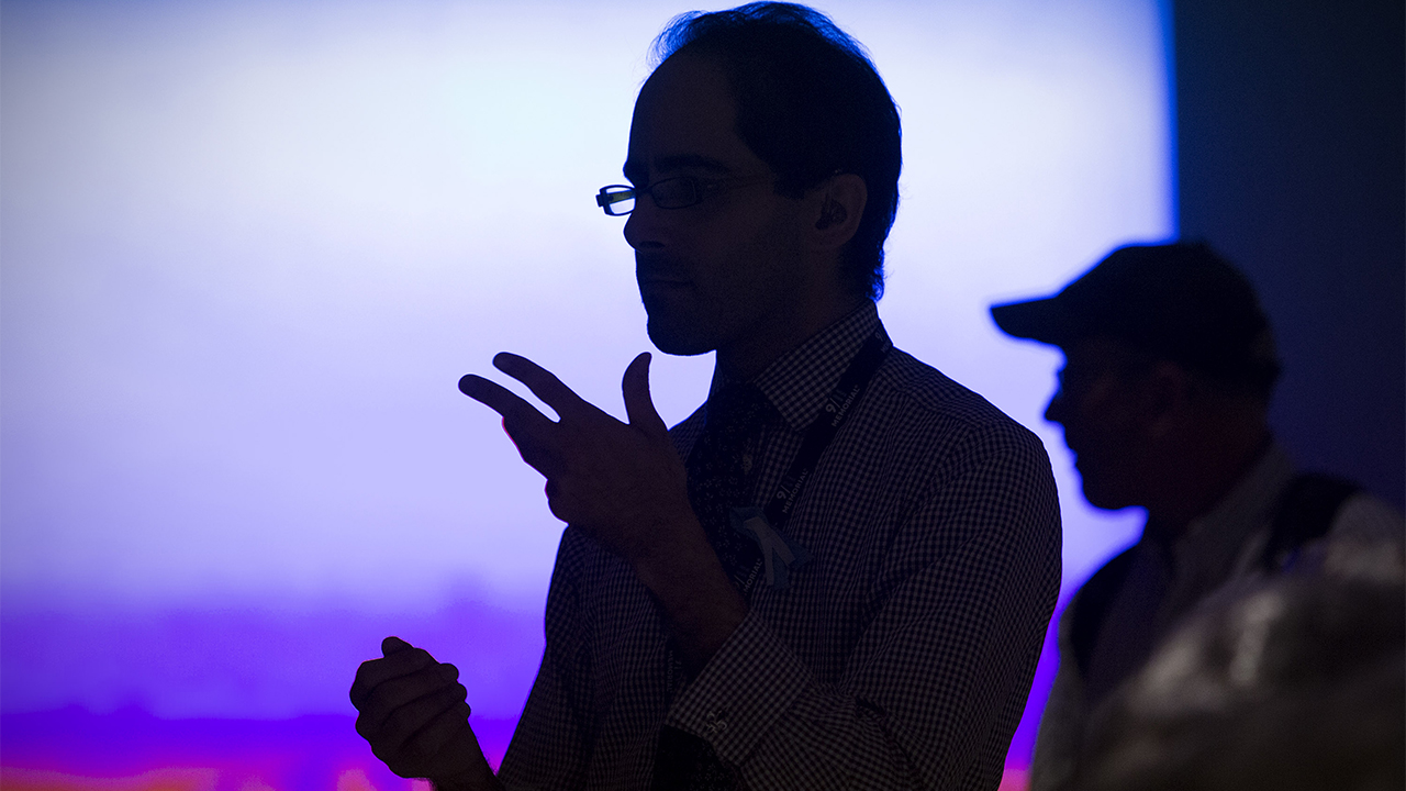 A man communicating in sign language is silhouetted against a bright screen at the Museum.