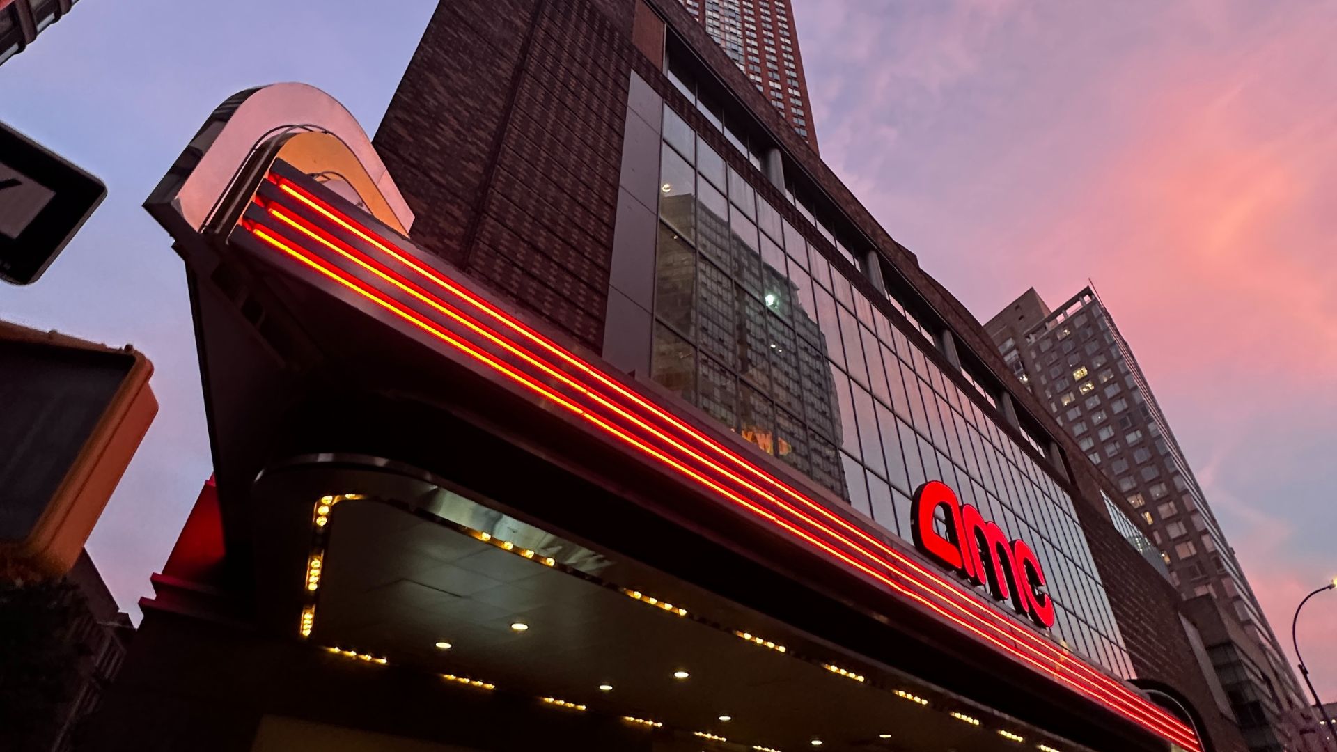 Exterior of an AMC Theater against a multi-colored pastel New York City sunset