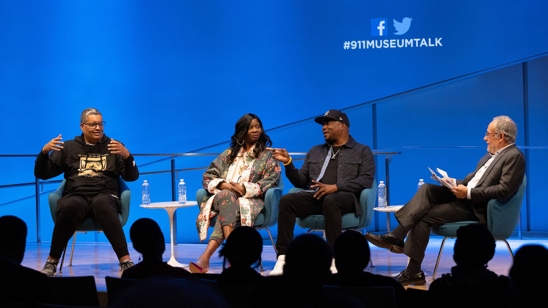 Panelists seated on stage, in conversation, against a dark blue curtain and the 9/11 Memorial & Museum logo.