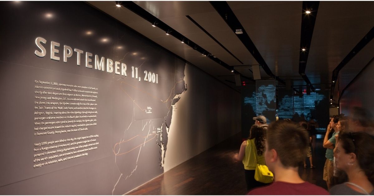 Visitors walk down a dimly lit hall. Beside them is a large map of the Eastern United States that shows the routes the hijacked planes took on 9/11.