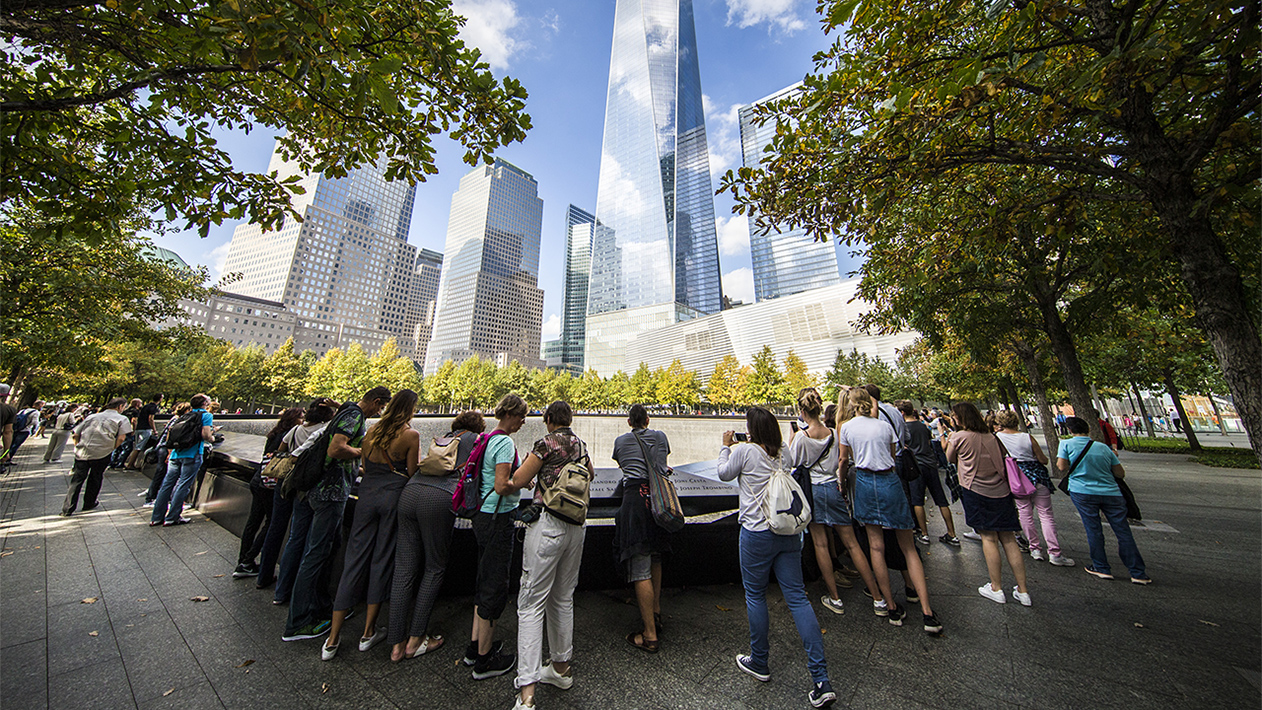 A group of students visits the 9/11 Memorial on a sunny day.