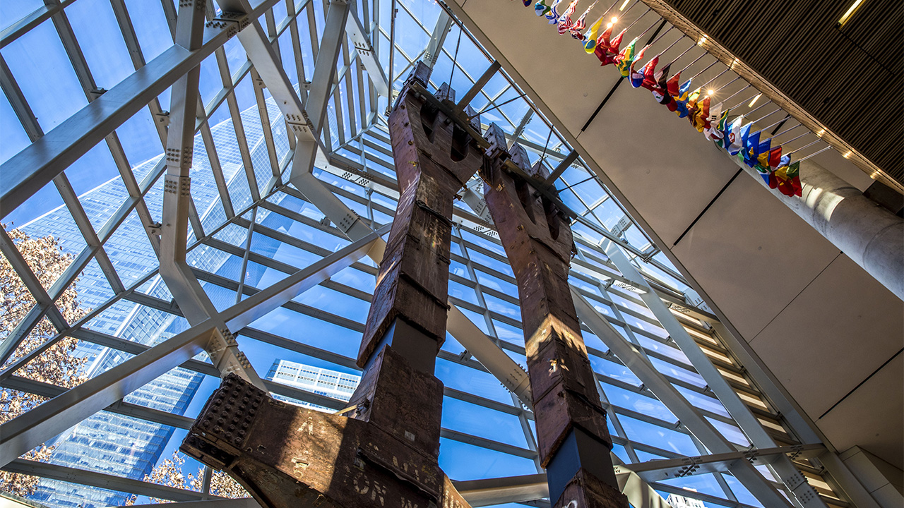 Two eighty-foot tall steel columns, known as the tridents, tower over the interior of the Museum pavilion. One World Trade Center stretches skyward outside the Museum windows.