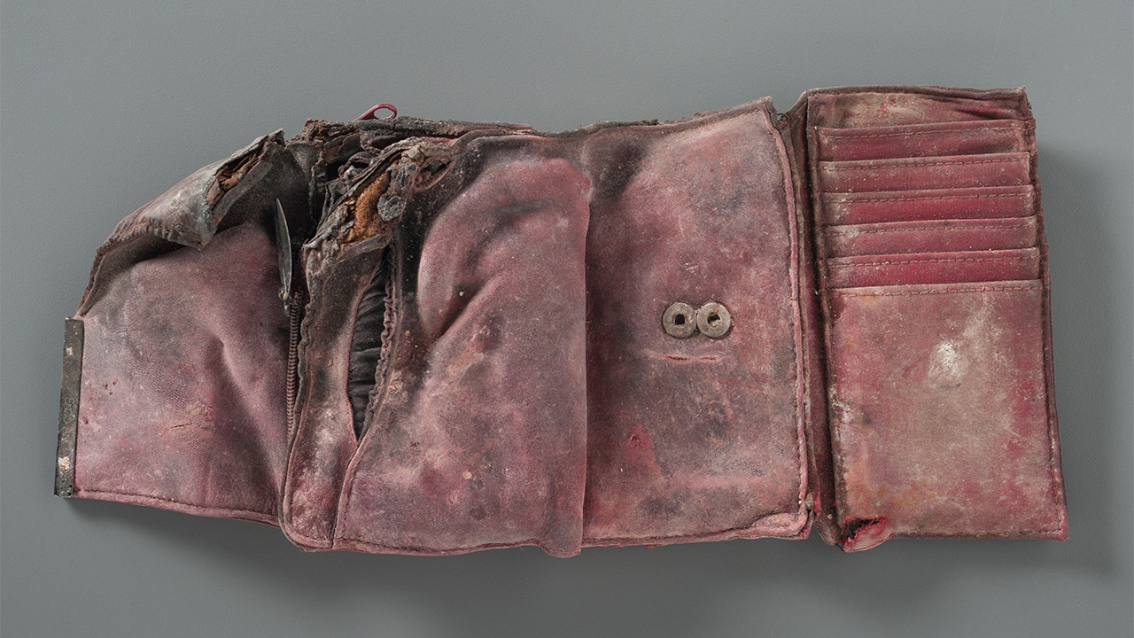A damaged and stained red wallet is open on a gray surface. The wallet is empty. Its left corner is burned and ripped.