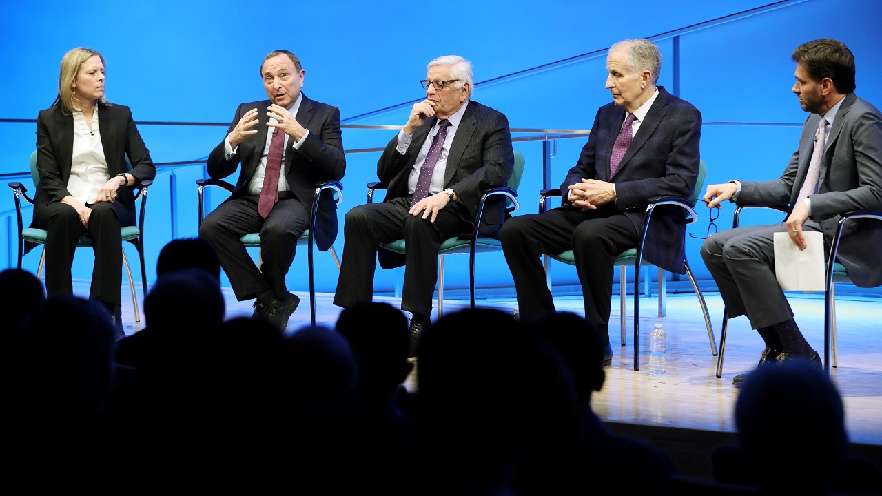 A woman and four men sit onstage while taking part in a public program about sports after 9/11 at the Museum Auditorium. To the left is WNBA Founding President and Big East Conference Commissioner Val Ackerman. To the right of her is NHL Commissioner Gary Bettman, who is speaking while gesturing with both hands. To the right of him is NBA Commissioner Emeritus David J. Stern. To the right of him is former NFL Commissioner Paul Tagliabue. At the far right is Mike Greenberg, longtime SportsCenter anchor and c