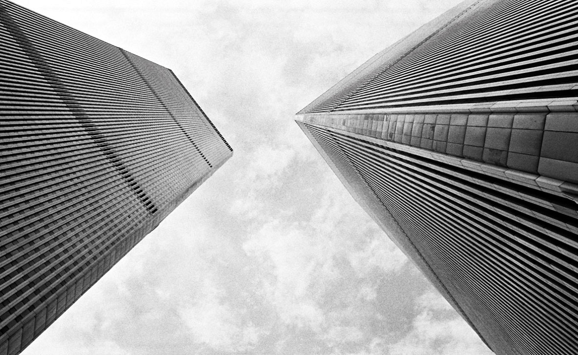 Low-angle view of the Twin Towers roaming into the cloudy sky. The height is emphasized by the towers' chamfered corners and closely spaced exterior columns.