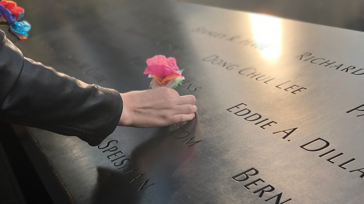 Image of a hand on a pink paper flower on a Memorial parapet