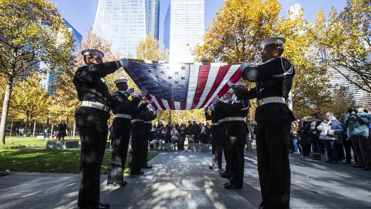 Uniformed military members hold an American flag