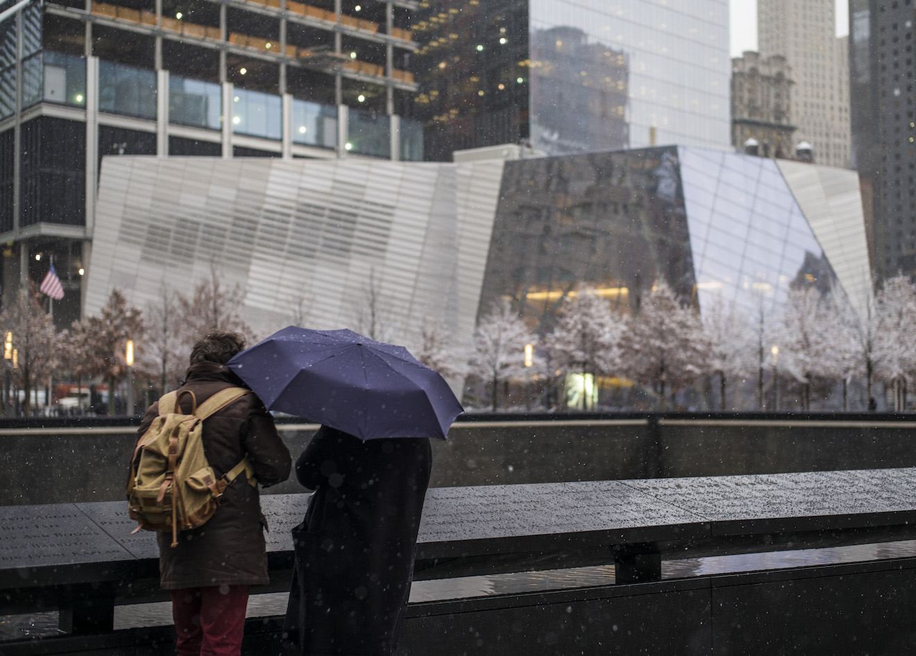 Visitors stand under an umbrella at the 9/11 Memorial 