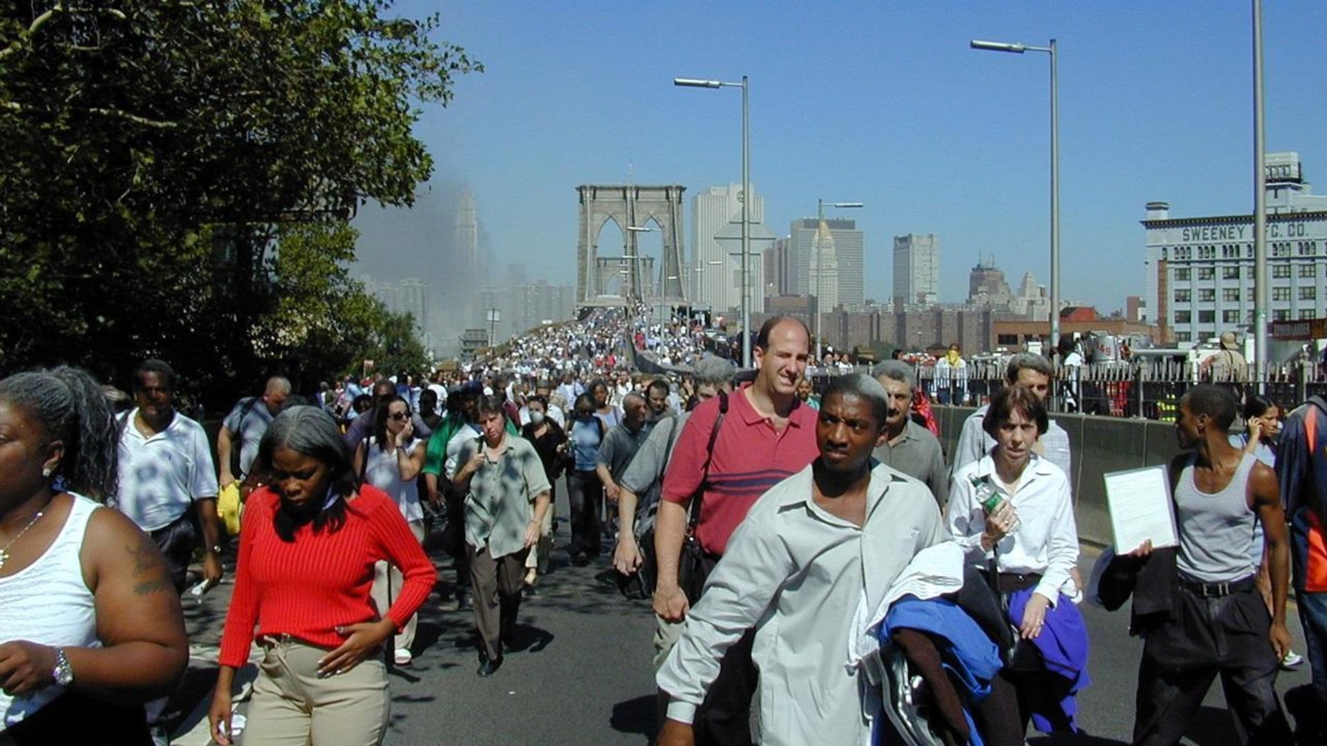 Crowds of people flee via the Brooklyn Bridge with lower Manhattan's smoke-covered skyline behind them 
