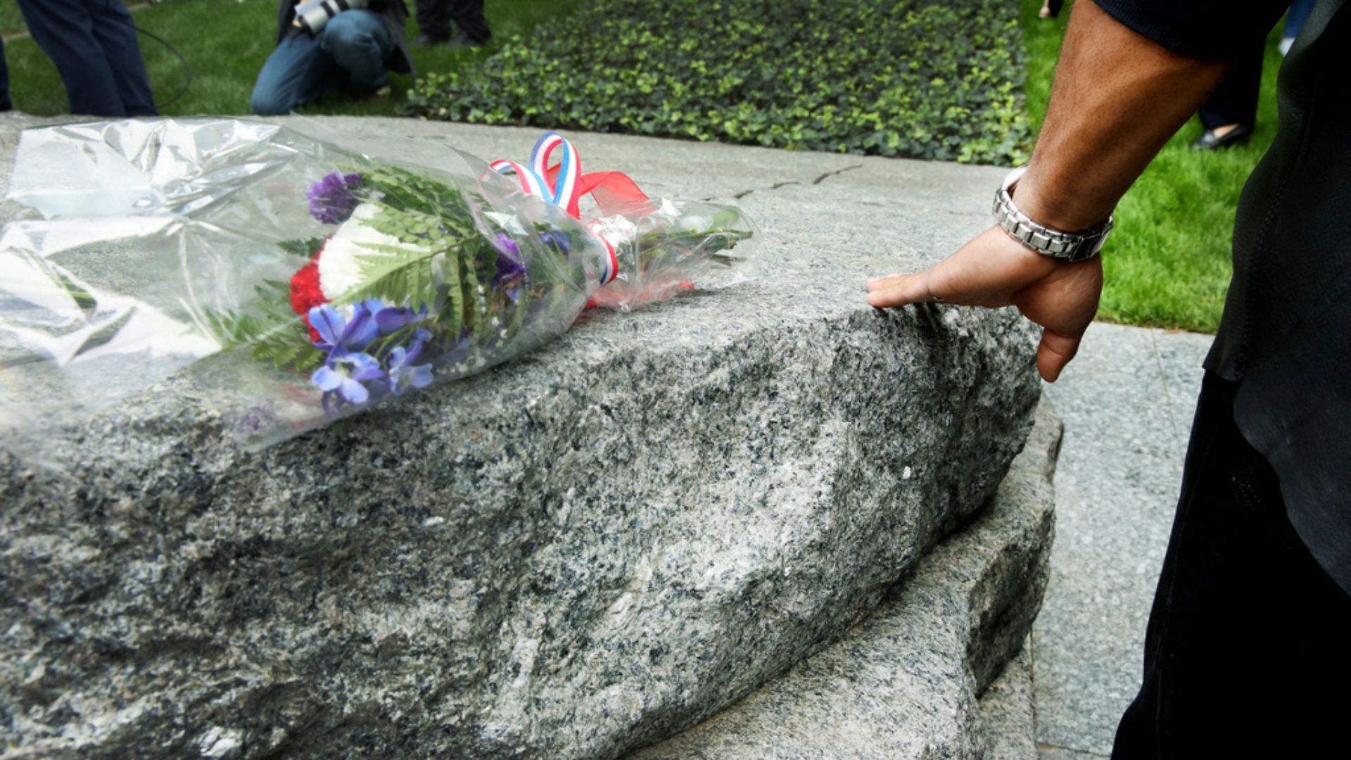 Bouquet of flowers on the Memorial glade, with a hand touching the stone