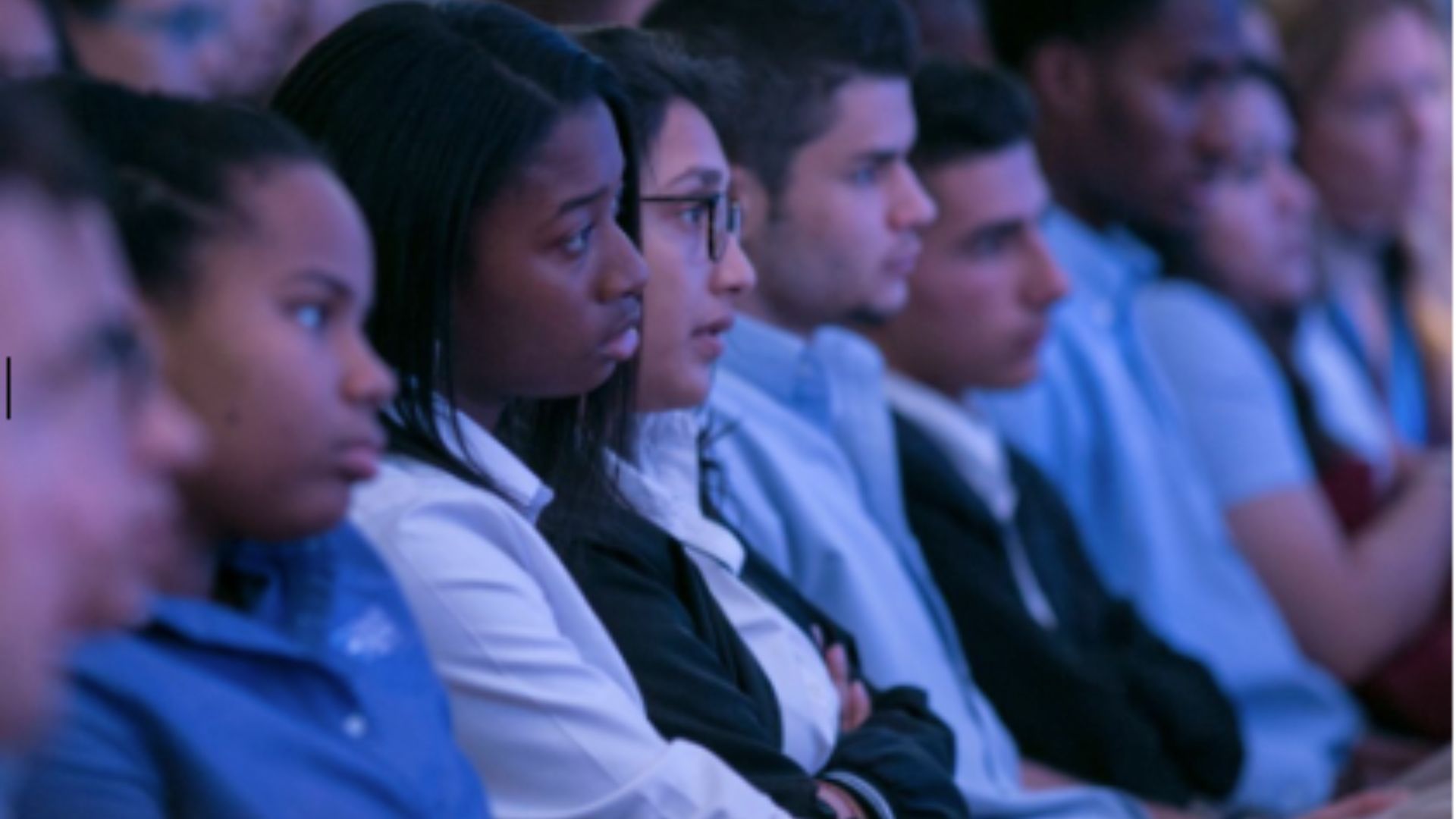 A group of students sit attentively in the Museum auditorium.