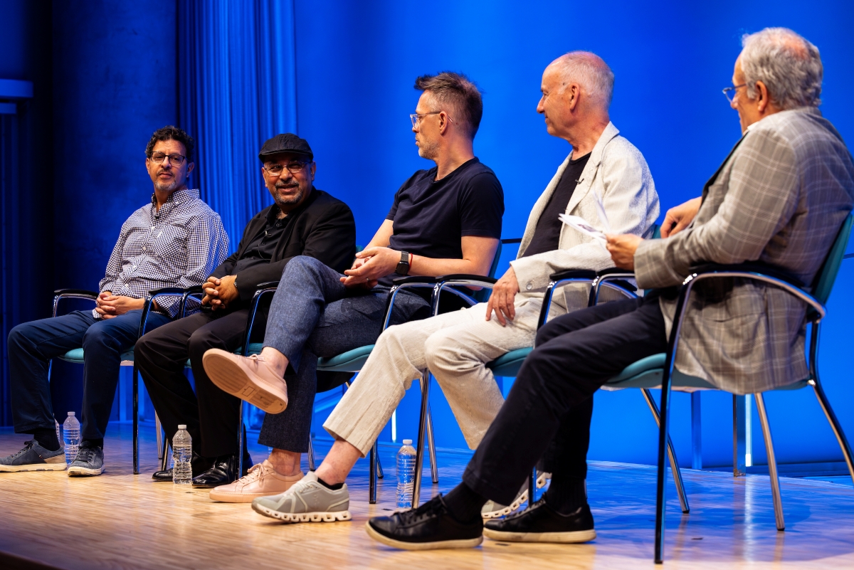 A panel sits on stage talking in front of a blue background