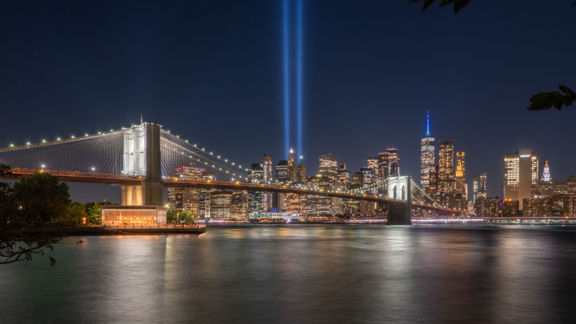 Twin beams of blue light rise from the New York City skyline, as seen across the river.
