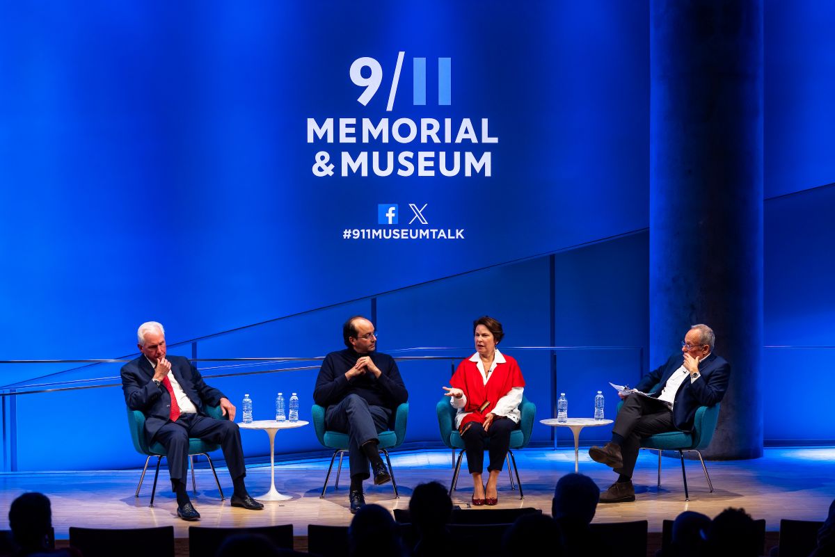 Panelists and moderator are sitting in front of a blue 911 logo on a stage