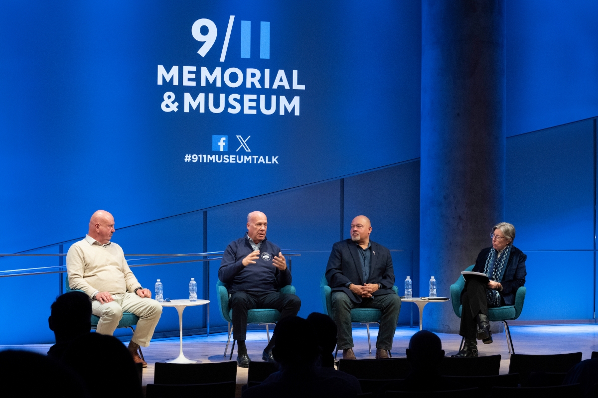 a group of people sit on stage under the 9/11 Memorial & Museum banner