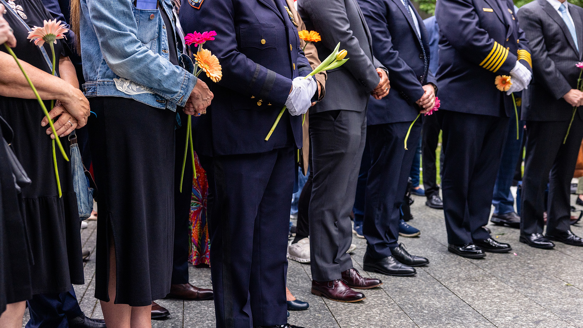 A group  of people, some in police dress uniform, solemnly clutch flowers.