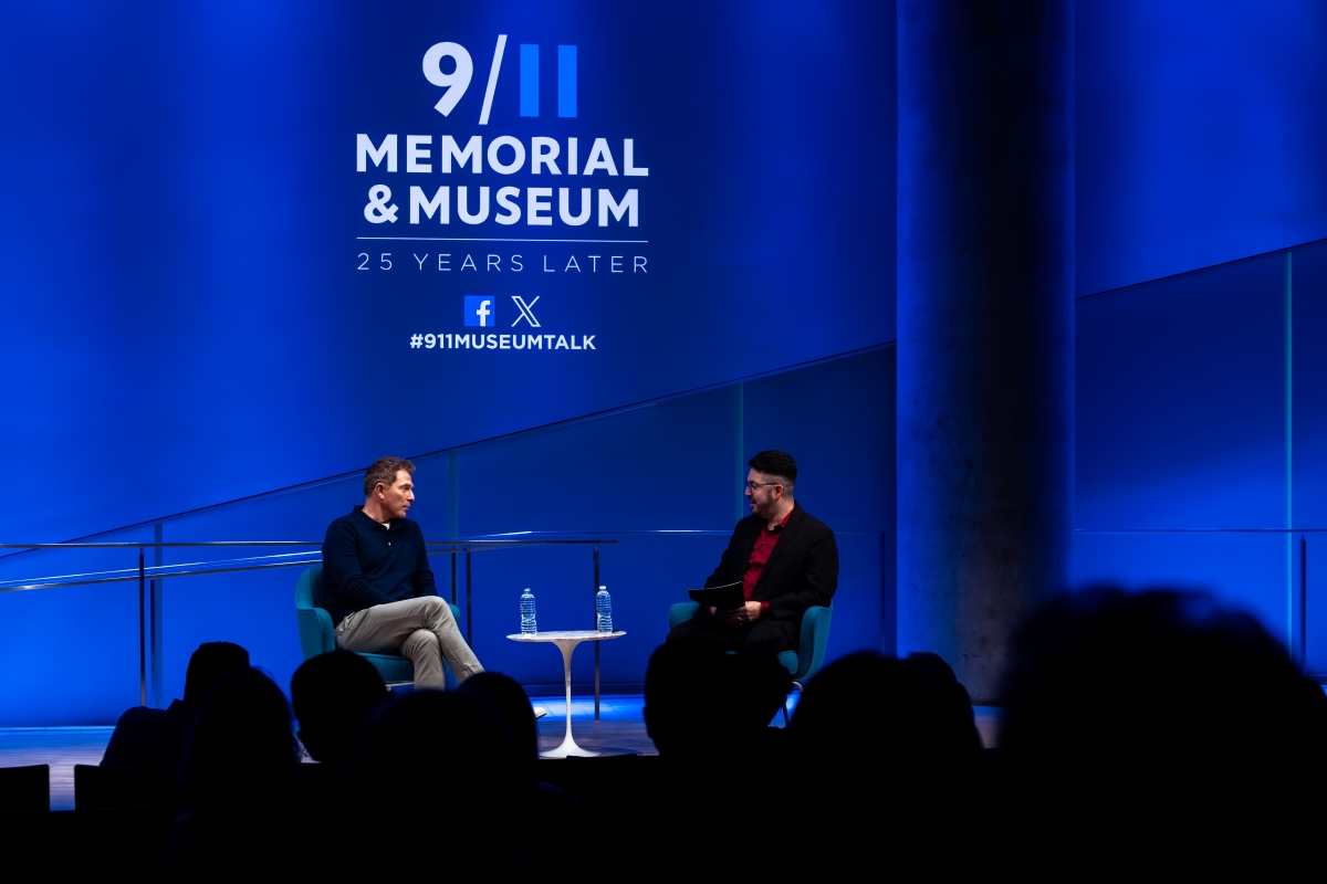 Bobby Flay and Alejandro Victoria sit on stage under the 911 Memorial and Museum logo