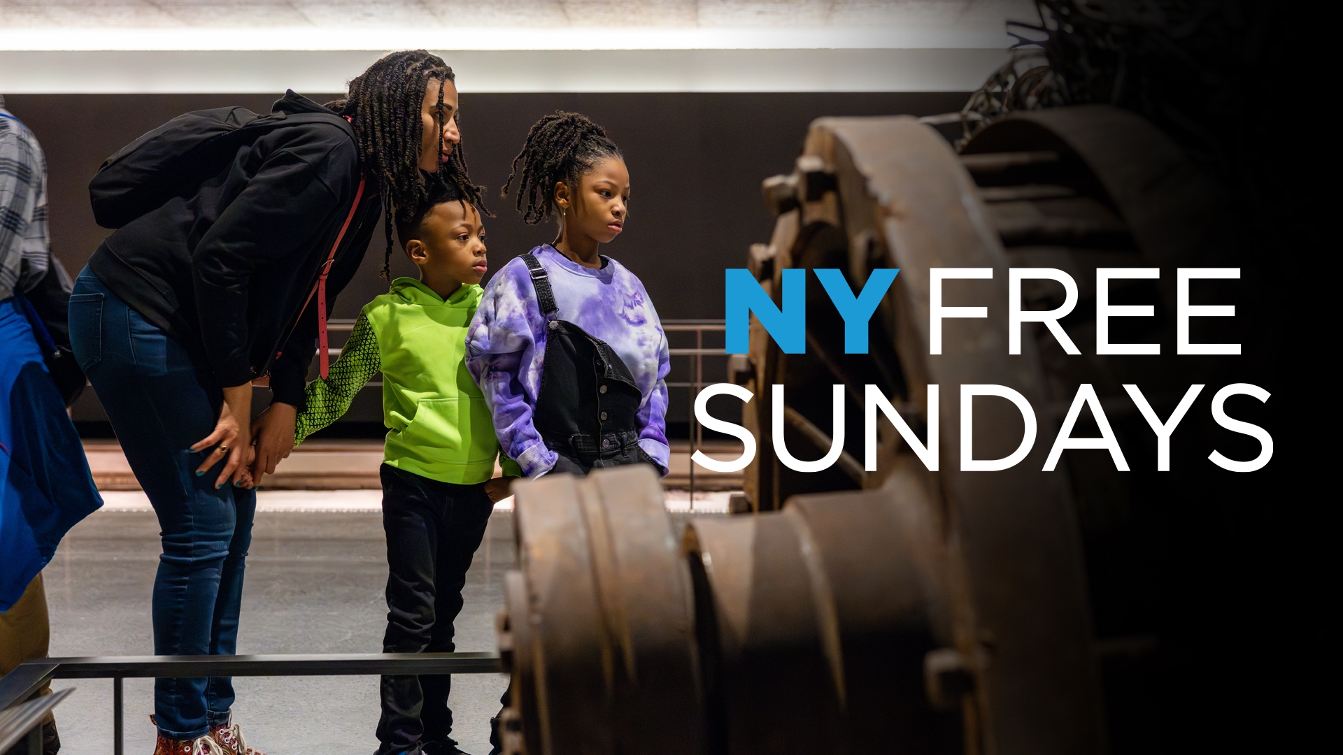 An adult leans down to talk to two children as they view an artifact. "NY First Sundays" overlays the artifact. 