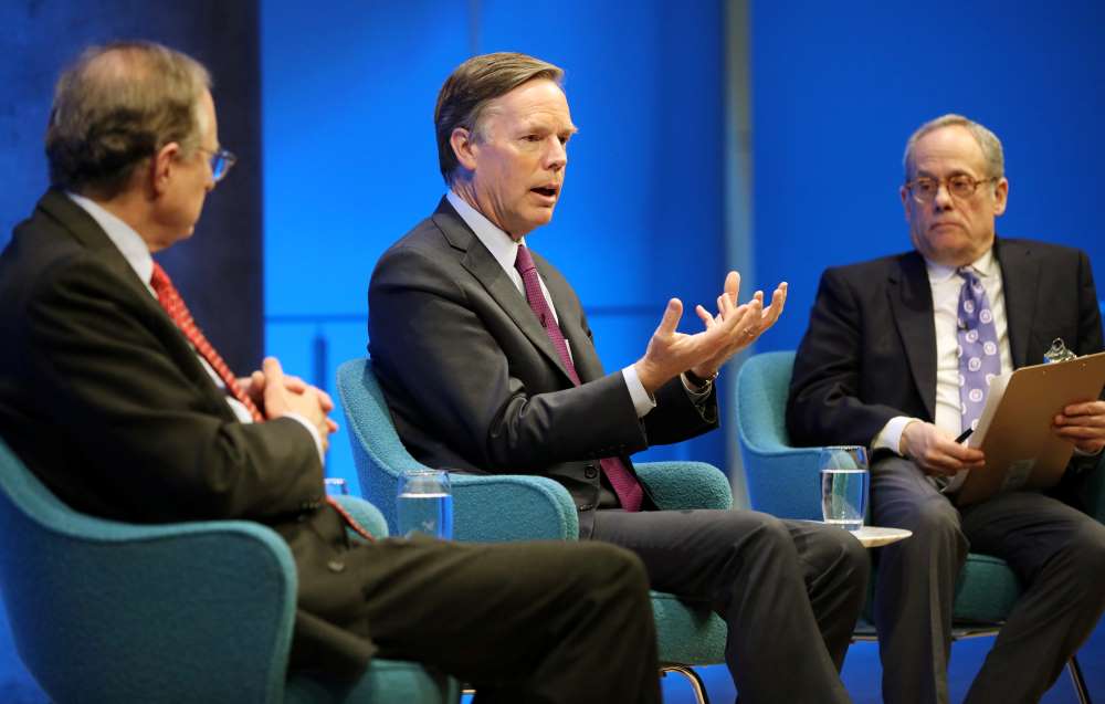 Former U.S. Ambassador to NATO R. Nicholas Burns gestures with both hands as he speaks onstage between former Deputy Secretary General of NATO Alexander Vershbow and Clifford Chanin, the executive vice president and deputy director for museum programs. Vershbow has his hands folded as he listens on. Chanin is holding a clipboard.
