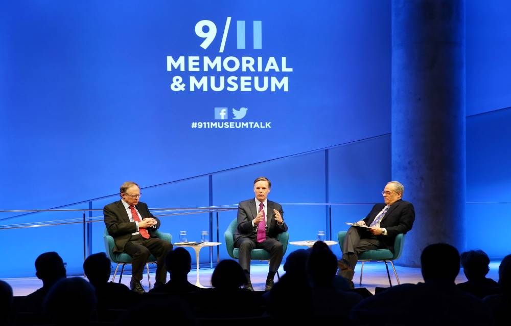 Former U.S. Ambassador to NATO R. Nicholas Burns and former Deputy Secretary General of NATO Alexander Vershbow are onstage during a public program in the Museum Auditorium. Clifford Chanin, the executive vice president and deputy director for museum programs is to the right of them seated and holding a clipboard. This wide-angle shot includes about a dozen audience members in the foreground, as well as a large 9/11 Memorial & Museum logo on the wall above the three men.