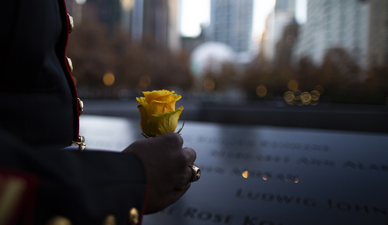 A man in dress uniform holds a yellow rose in his hand with the Memorial parapet in the background.