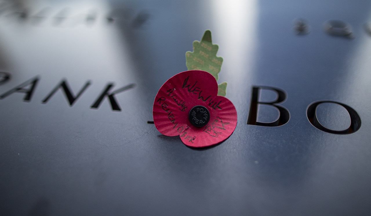 A paper poppy flower is left on the Memorial parapet.