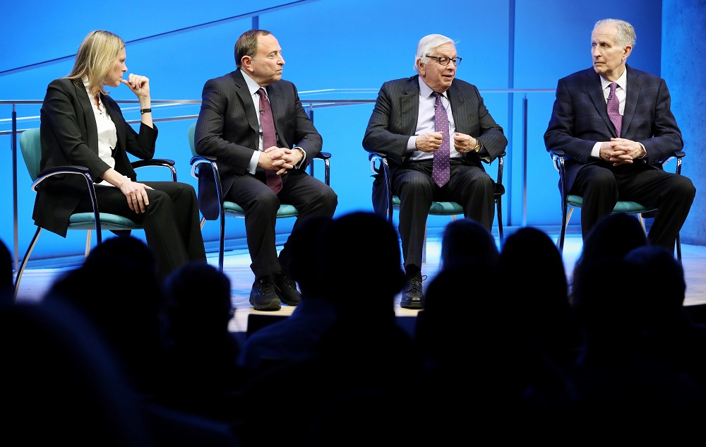 NBA Commissioner Emeritus David J. Stern speaks onstage at the Museum Auditorium. To his left is former NFL Commissioner Paul Tagliabue. To his right are WNBA Founding President and Big East Conference Commissioner Val Ackerman and current NHL Commissioner Gary Bettman. Stern is speaking while gesturing with both hands and looking out at the audience, which is silhouetted by the stage lights.