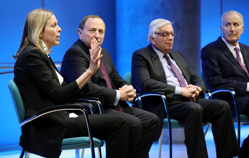 WNBA Founding President and Big East Conference Commissioner Val Ackerman speaks onstage at the Museum Auditorium. She holds up both hands as she looks out at the audience. To the right of her are NHL Commissioner Gary Bettman, NBA Commissioner Emeritus David J. Stern, and former NFL Commissioner Paul Tagliabue.