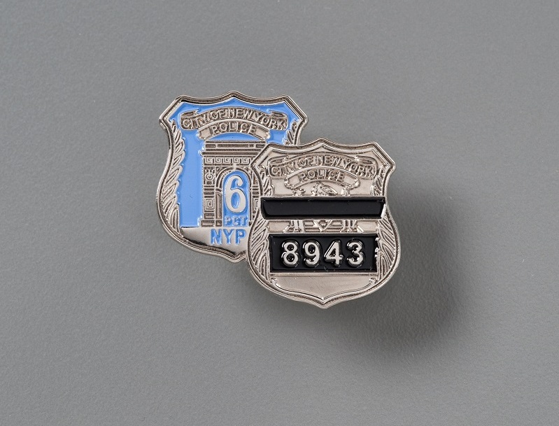 Two NYPD metal shield badges. One with the numbers '8943' written on black bar and the other with the number 6 written on light blue background.