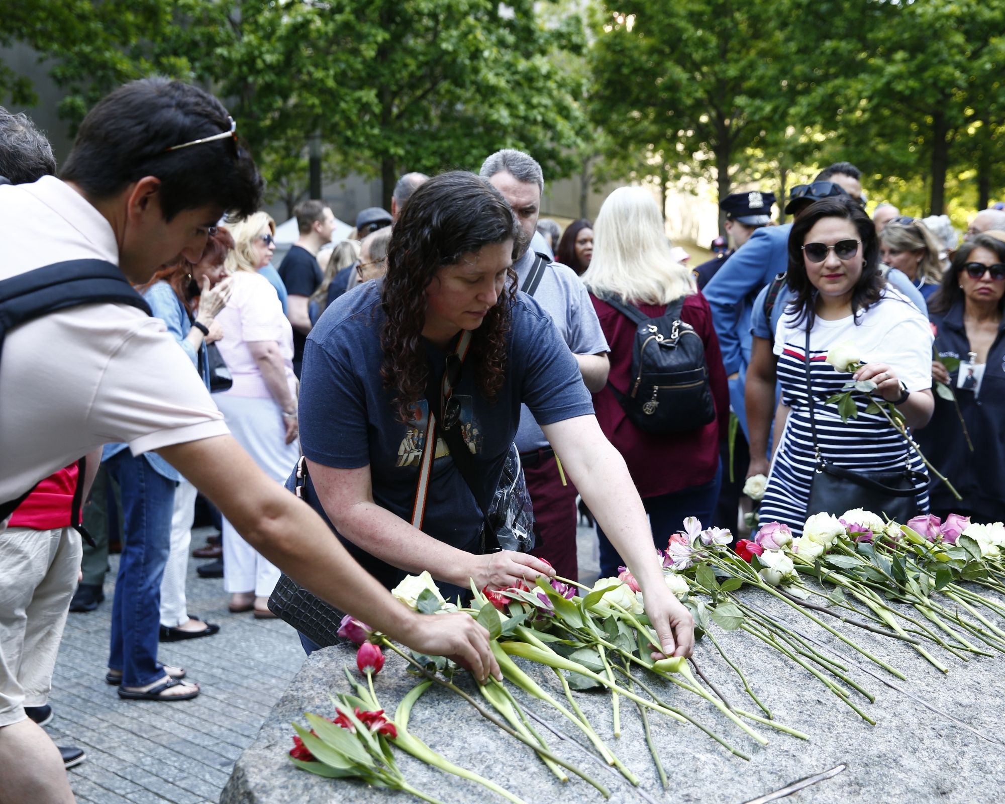 A group of people wearing short sleeves lay flowers on the Memorial Glade