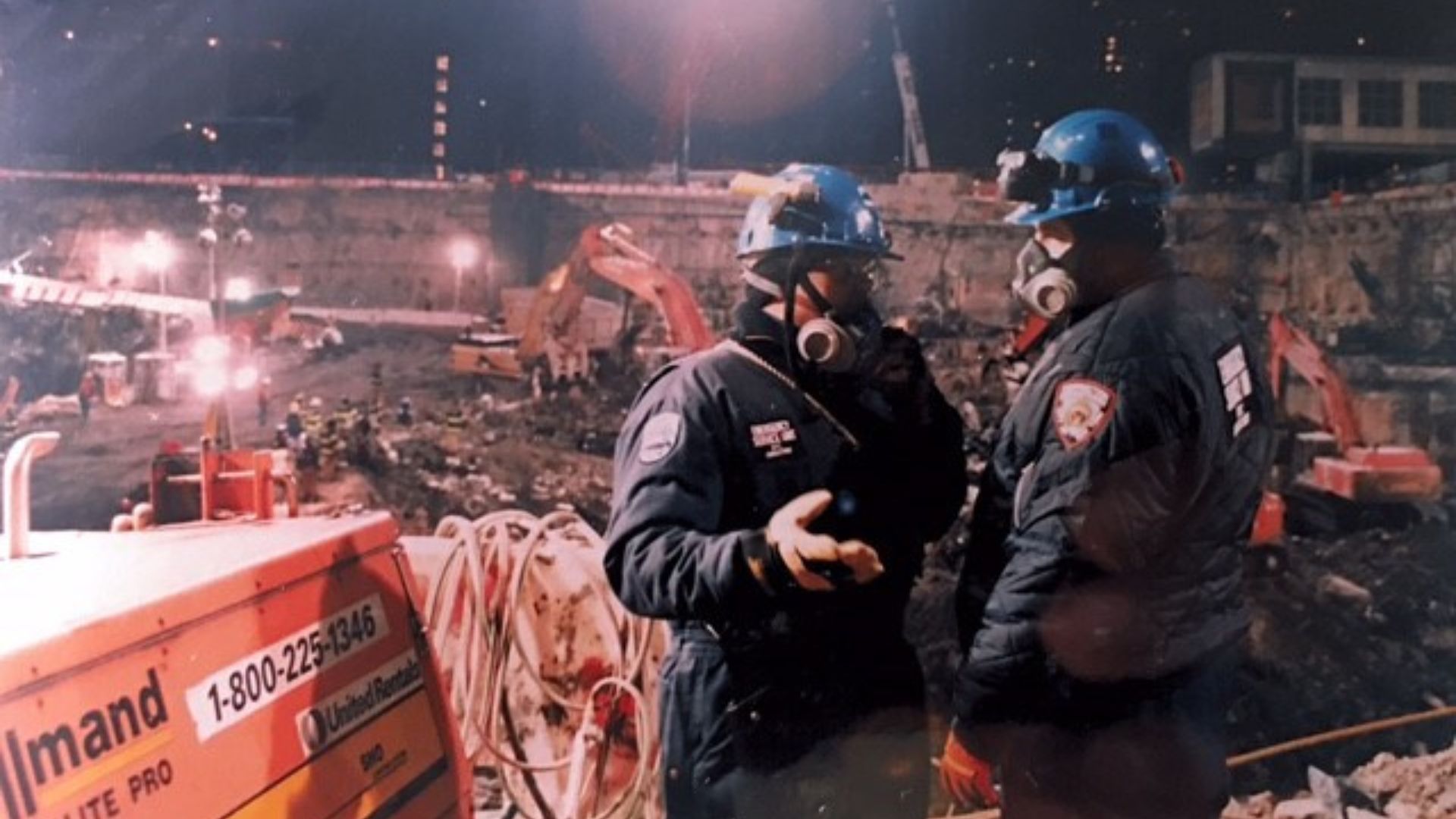Department of Correction workers speak with protective face masks at Ground Zero. Cranes are visible in the background. 