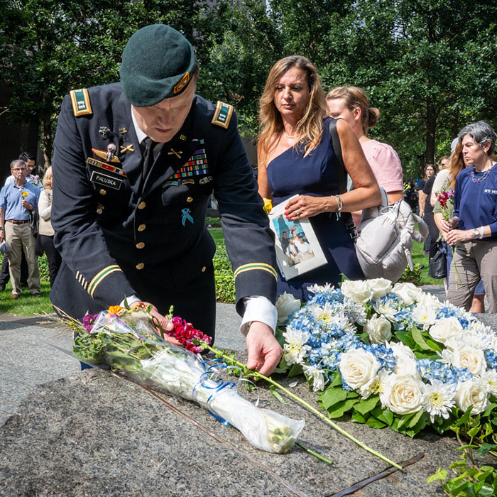 a uniformed service member lays a flower on a monolith
