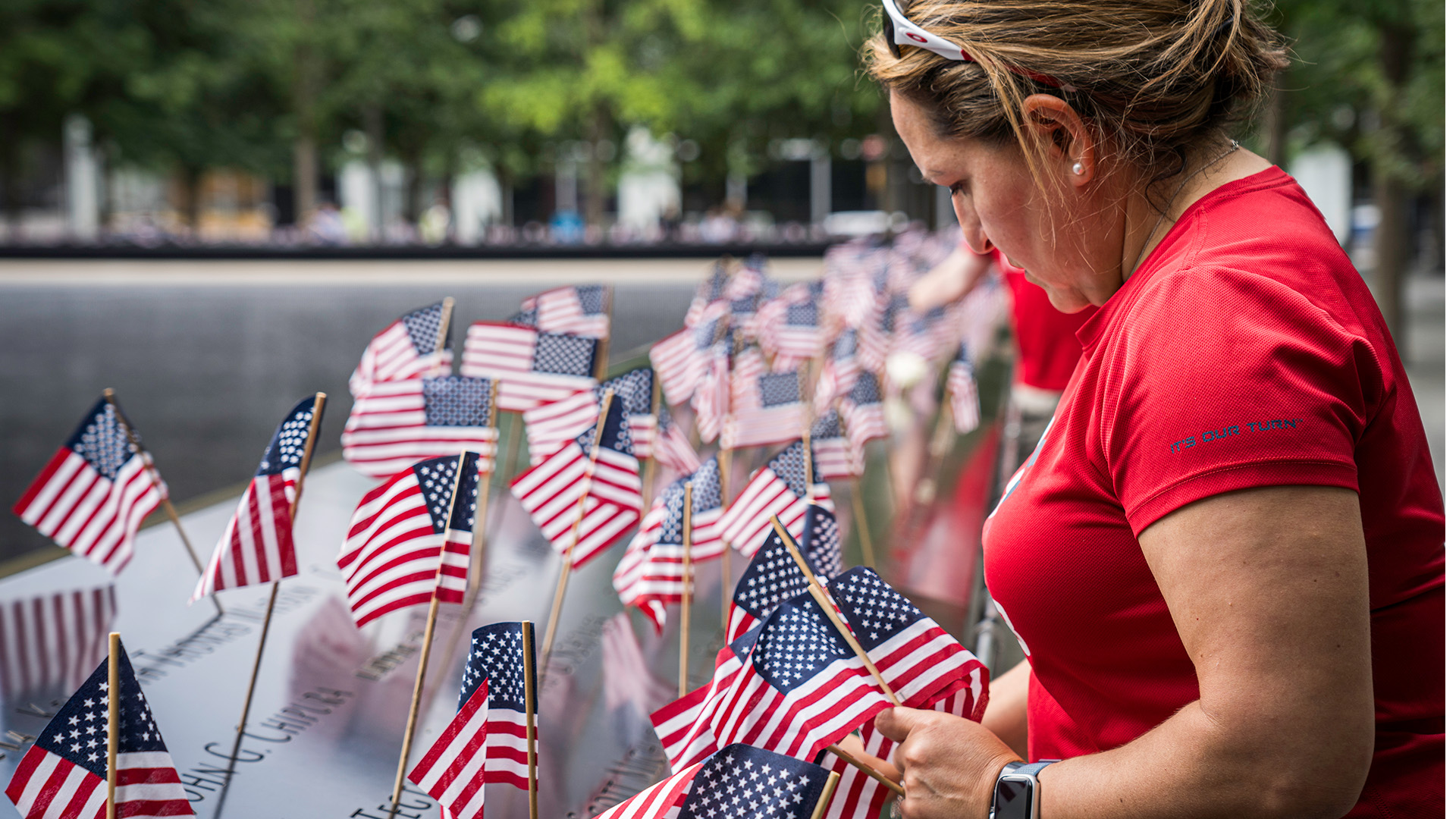 A woman in a red top leans over the 9/11 Memorial, which is lined with small American flags at each victim's name
