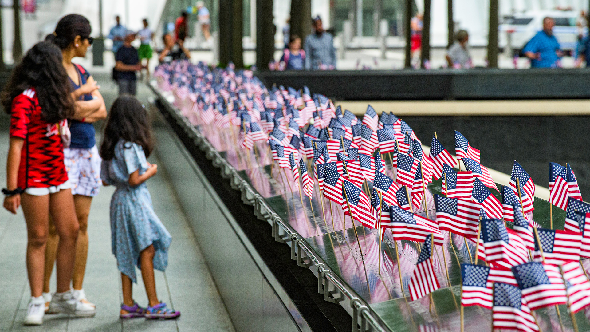 A woman and two younger girls look on at the Memorial, which is lined with small American flags at each victim's name