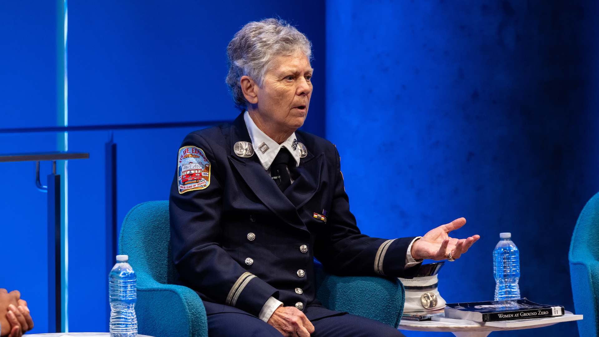 Captain Brenda Berkman sits in a chair with one palm up, midspeech