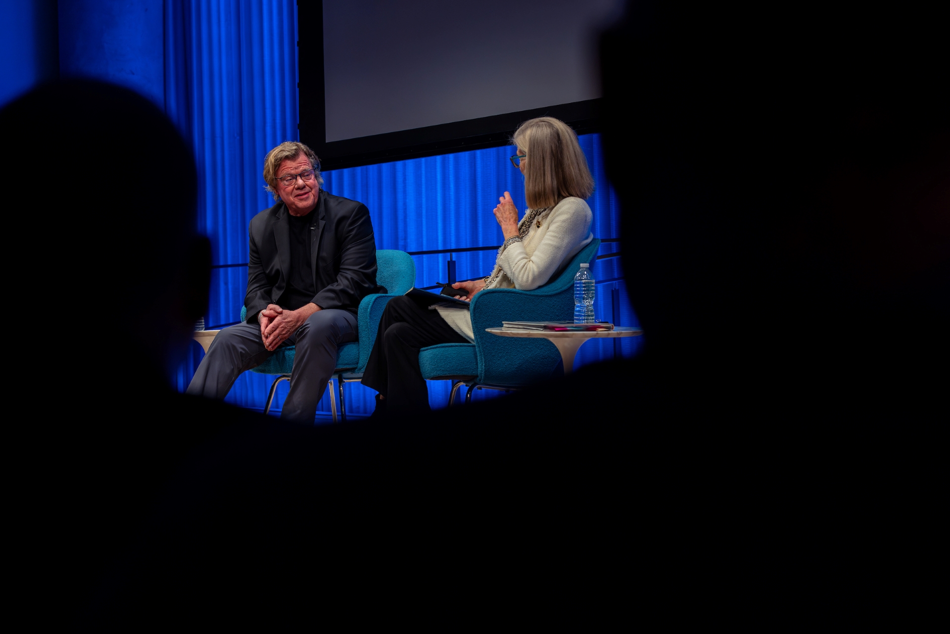 Joe McNally and Jan Ramirez on stage, seen from the side, between the darkened shadows of two audience members. 