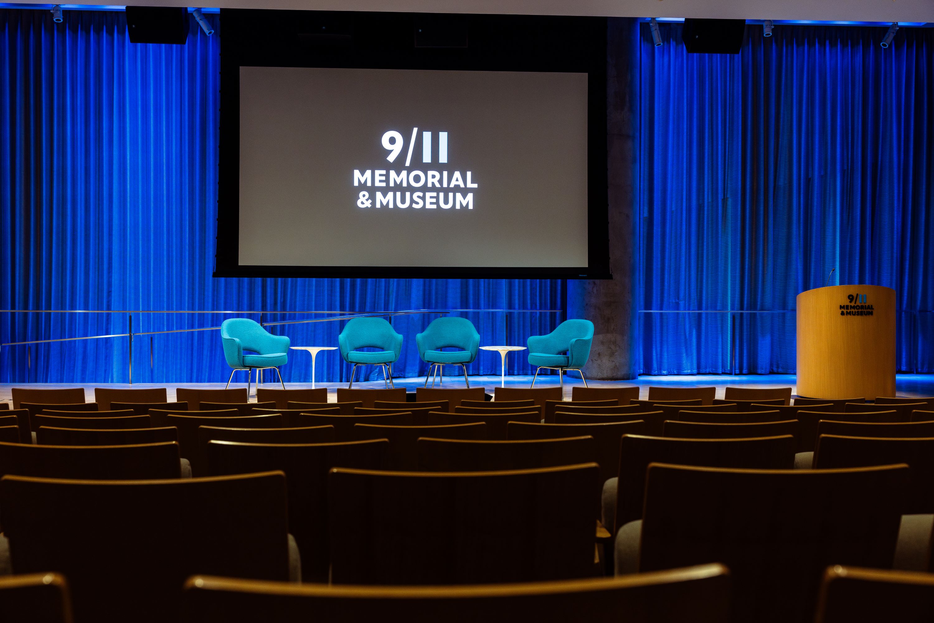 Auditorium stage with podium, chairs and the 9/11 logo on a screen