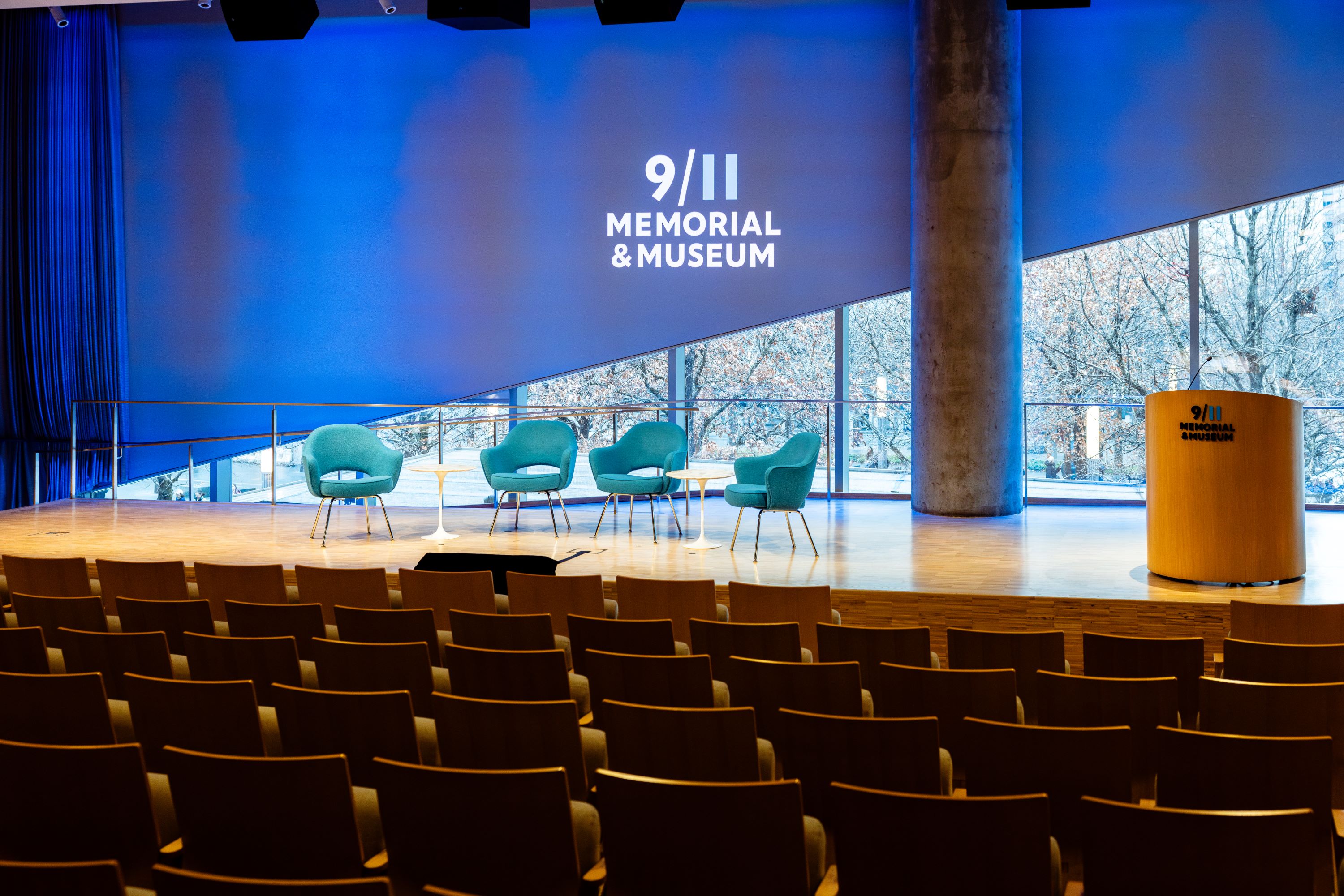 day time shot of the auditorium with the blue blinds partially raised at an angle allowing light to filter in from behind the stage